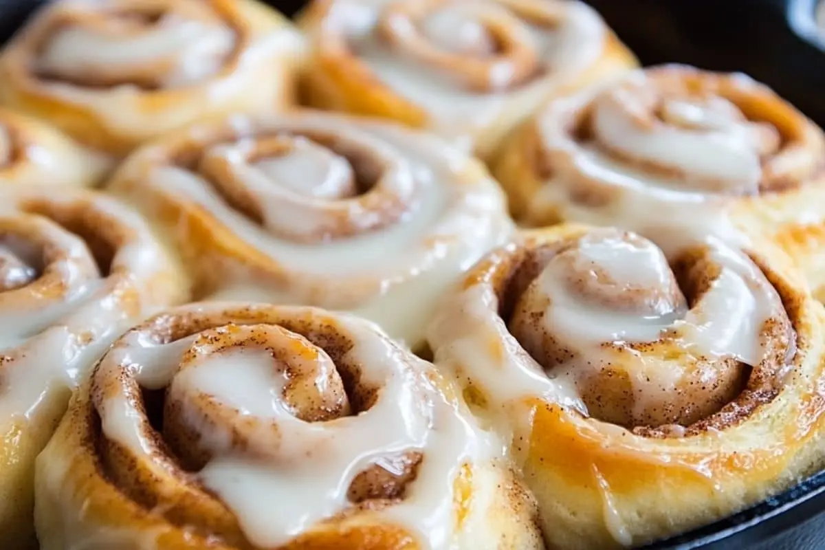 Freshly baked sourdough cinnamon roll recipe​ in a cast iron skillet, covered with creamy white frosting.