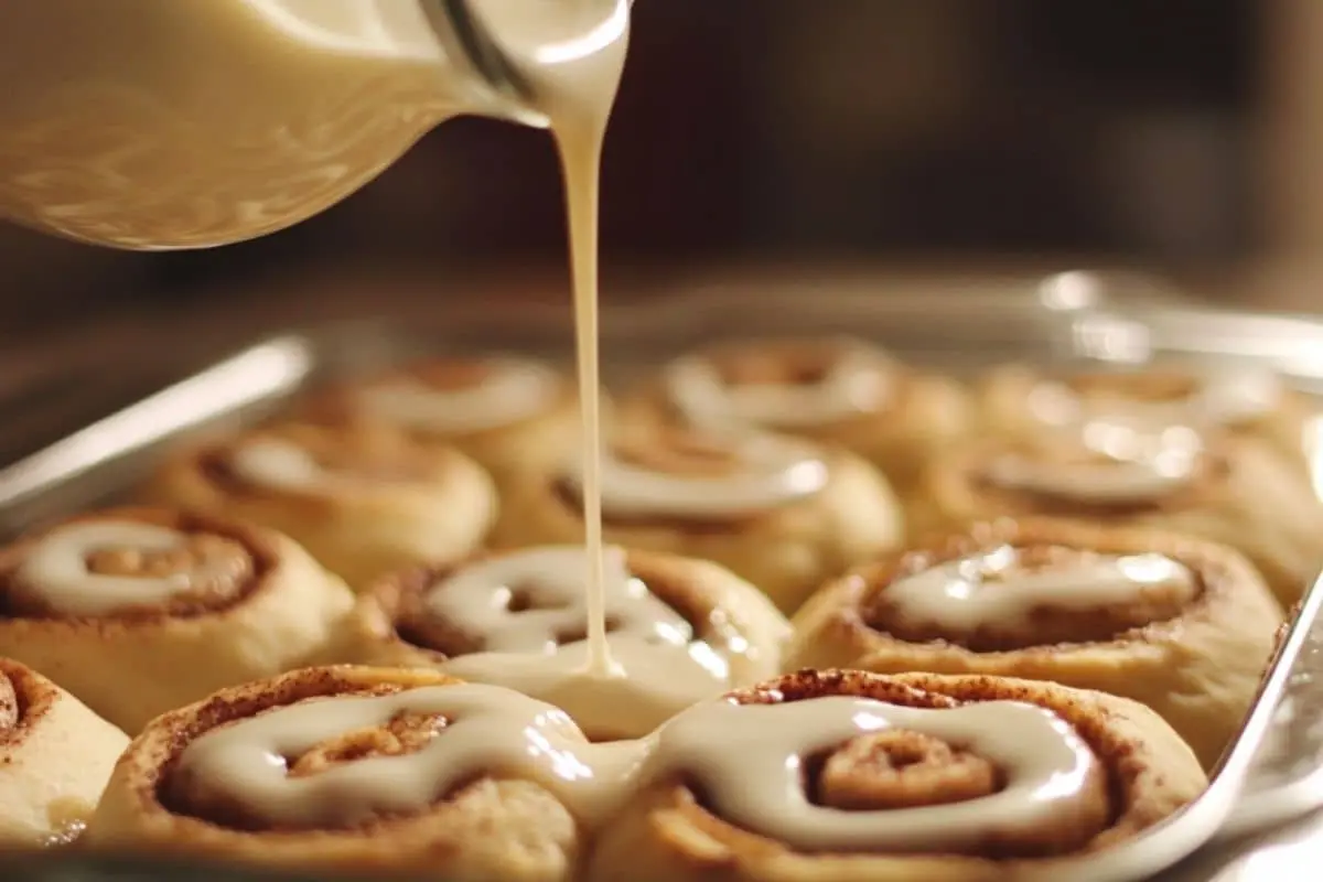 Raw cinnamon rolls in a baking dish with heavy cream being poured over them.