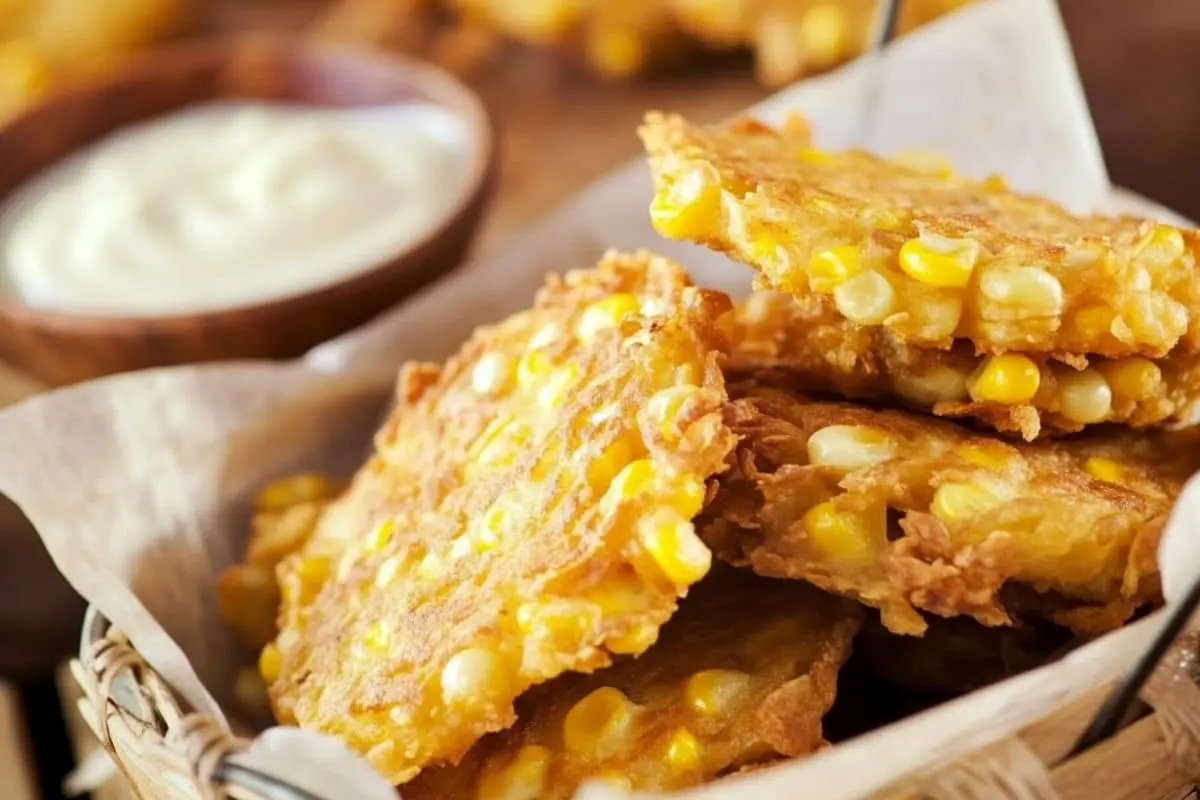 A basket of crispy, golden corn fritters with a side of dipping sauce.