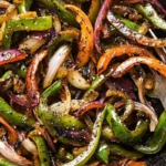 A close-up of sautéed Chipotle fajita veggies with green bell peppers, red onions, and orange bell peppers in a skillet, glistening with seasoning