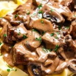 A bowl of creamy vegan beef stroganoff served over wide egg-free noodles, garnished with fresh parsley.