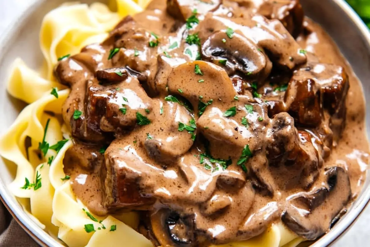 A bowl of creamy vegan beef stroganoff served over wide egg-free noodles, garnished with fresh parsley.